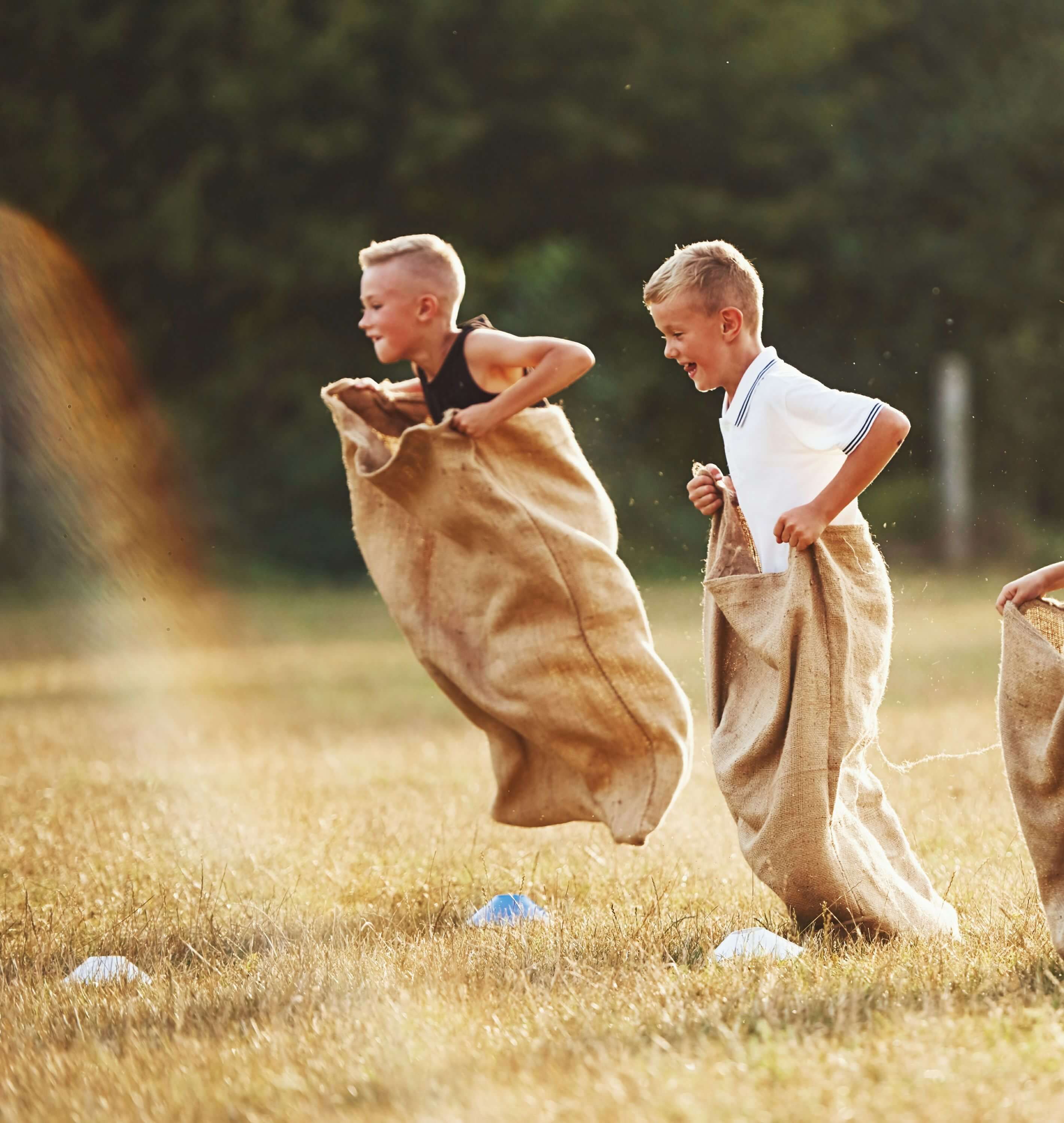 2 Jungen sind auf einer Wiese und machen Sackhüpfen
