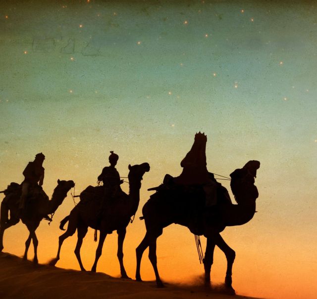 Silhouetten von 3 Kamelen mit je einem Menschen drauf vor einem rot-grün-blauen Nachthimmel.