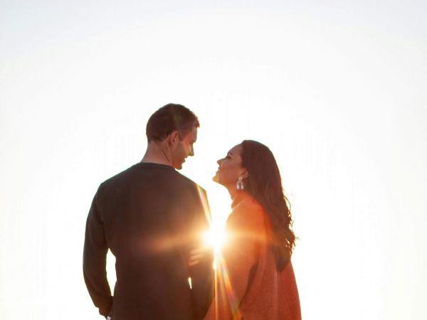Ein junges Paar steht auf einer Wiese vor einem Berg und die Sonnenstrahlen  strahlen zwischen ihnen durch.