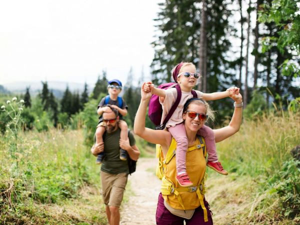 4-köpfige Familie im Wald. Die Kinder sitzen auf den Schultern der Eltern. Alle tragen Sonnenbrillen.