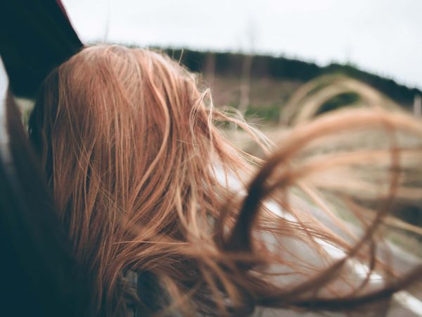 Eine weibliche Person schaut aus dem Fenster eines fahrenden Autos. Die Haare wehen im Wind.