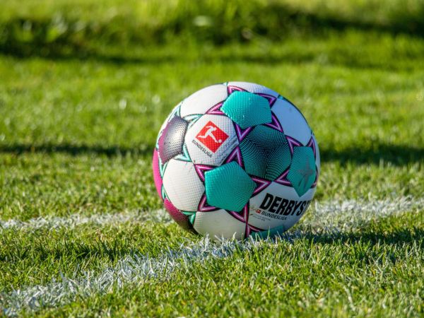 Auf einem grünen Rasen, mit weißer Markierung,  liegt ein bunter Fußball.