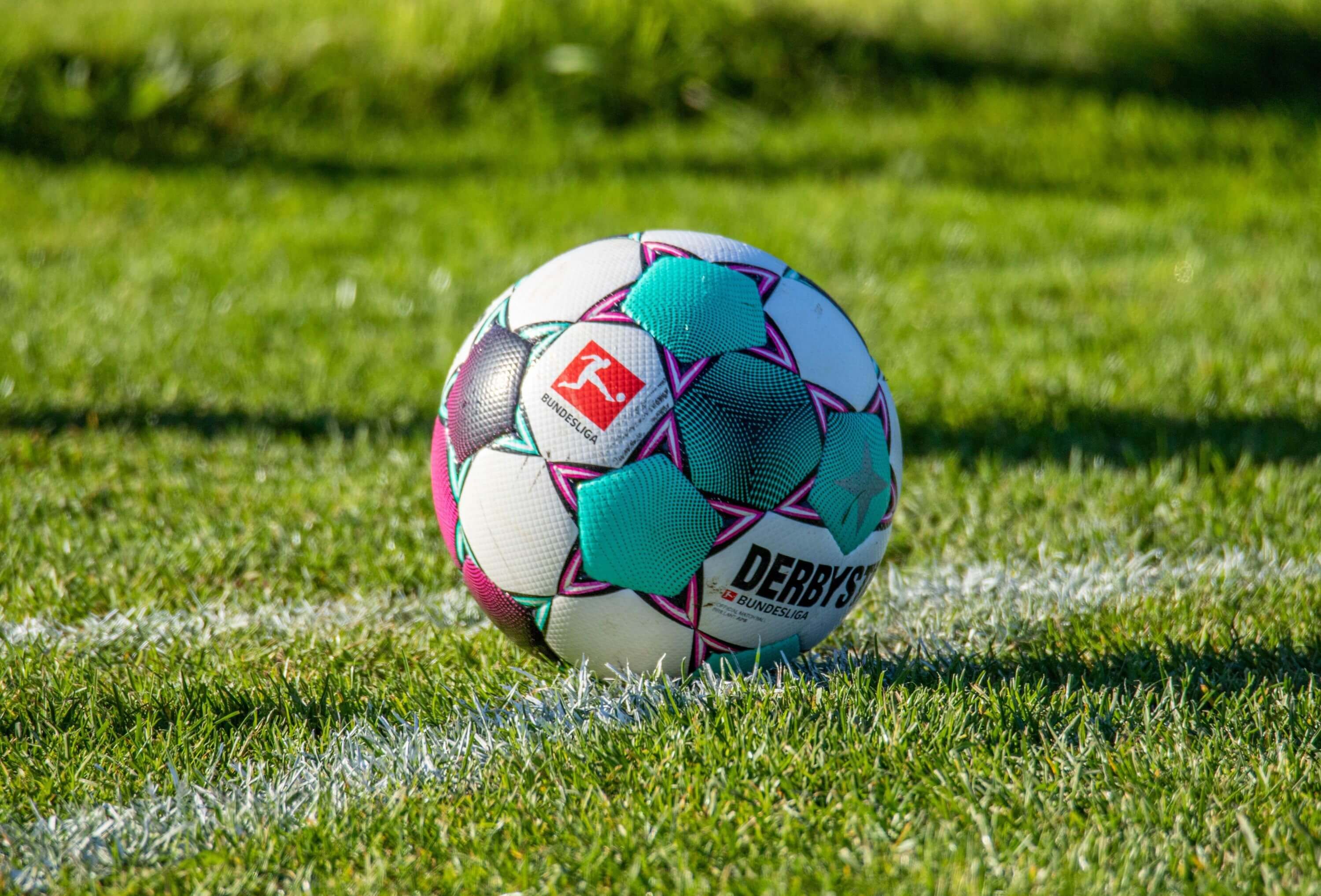 Auf einem grünen Rasen, mit weißer Markierung,  liegt ein bunter Fußball.