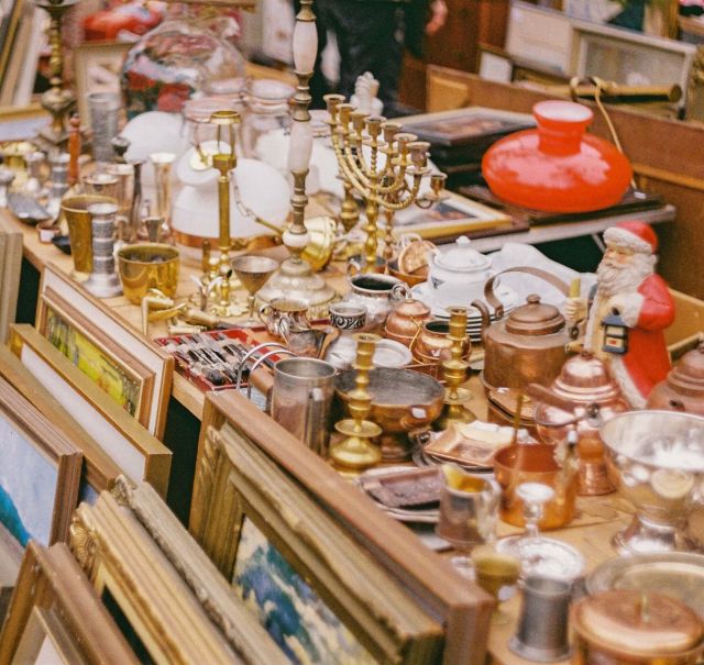 Ein Flohmarkt-Stand auf dem viele Gegenstände zum Verkauf stehen. Z.B. gerahmte Bilder, Leuchter usw.