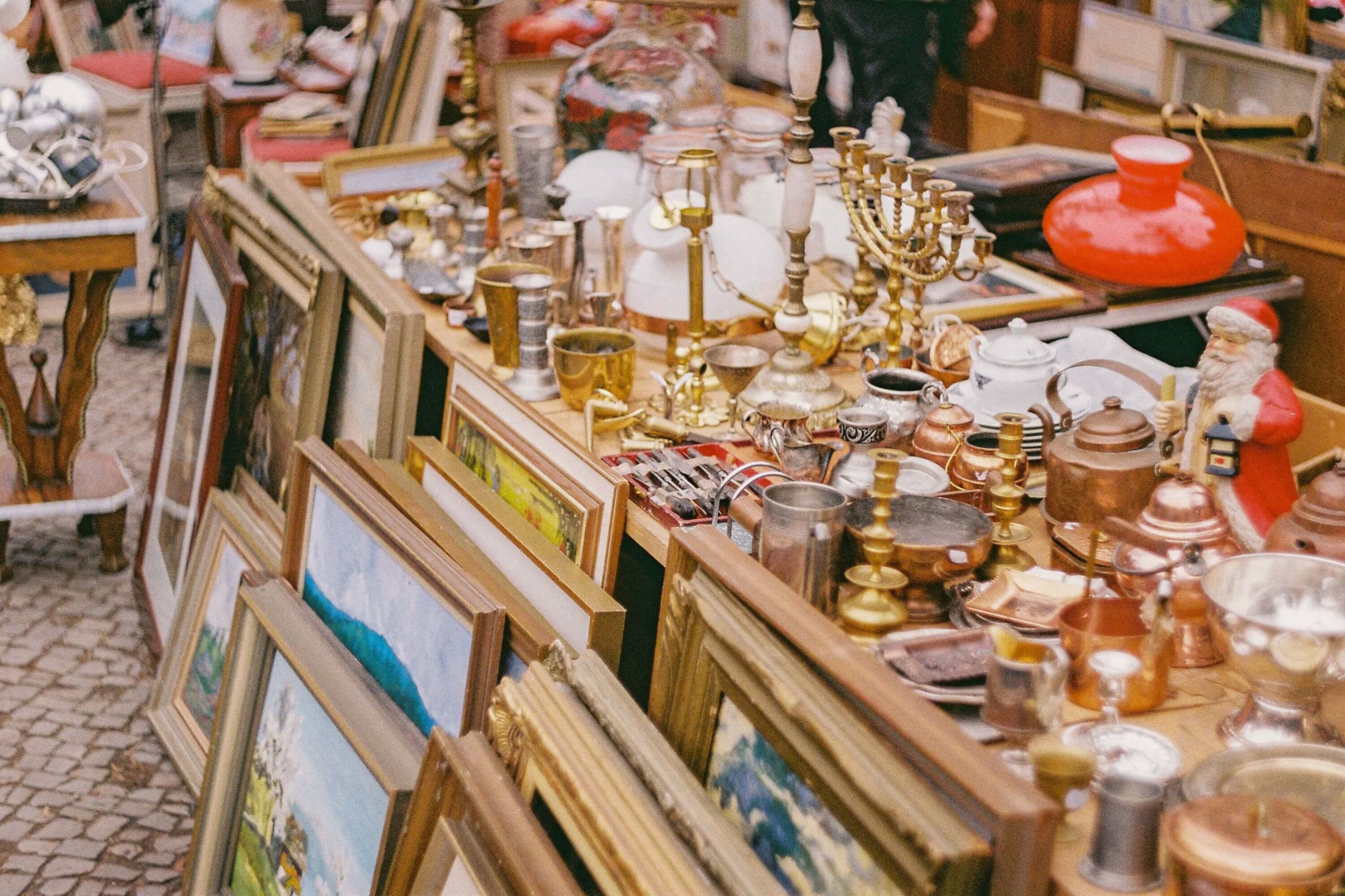 Ein Flohmarkt-Stand auf dem viele Gegenstände zum Verkauf stehen. Z.B. gerahmte Bilder, Leuchter usw.