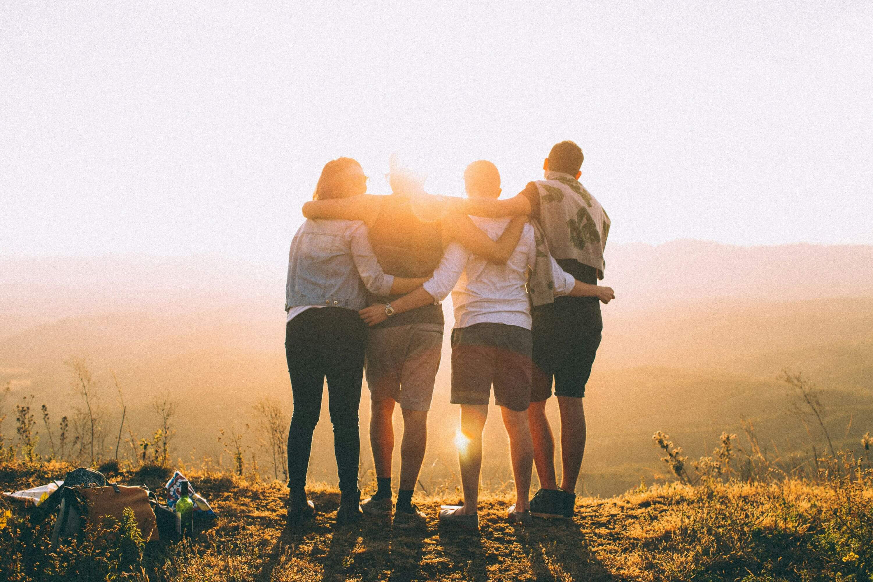 Jugendfreizeit 2026 4 Jugendliche stehen in einer Reihe auf einem Berg und lege sich die Arme über die Schultern. Sie sind mit dem Rücken zu sehen und schauen sich den Sonnenuntergang an.